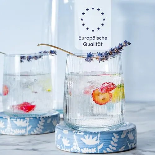 Zwei geriffelte Gläser mit Eiswasser, Beeren und Lavendel auf blauen Untersetzern