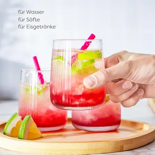 Hand greift ein geriffeltes Glas mit rotem Eisgetränk, Limette auf Holztablett